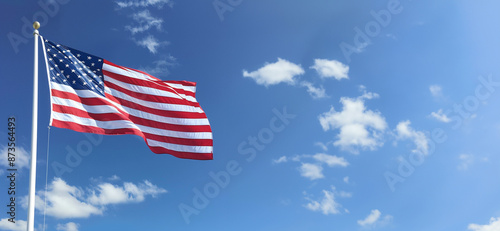 Fototapeta Naklejka Na Ścianę i Meble -  American flag on flag pole flying in the wind against blue sky with clouds 