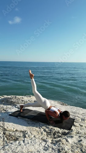  beautiful girl in white sports clothes does yoga in nature, performs asanas and balance stands among white rocks against the background of the sea