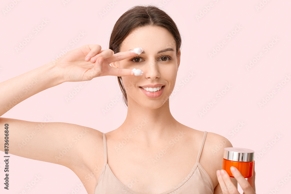 Beautiful young woman with cream on fingers holding jar of sunscreen against pink background Beautiful young woman with cream on fingers holding jar of sunscreen against pink background