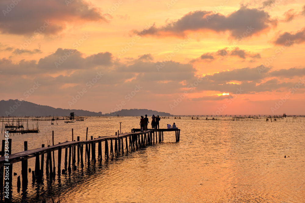 Golden hues of sunset paint the sky and reflect on the tranquil waters, creating a serene and picturesque scene by the pier Golden hues of sunset paint the sky and reflect on the tranquil waters, creating a serene and picturesque scene by the pier