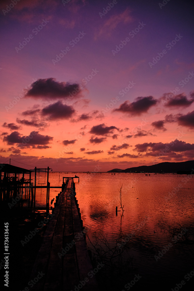 Obraz premium Golden hues of sunset paint the sky and reflect on the tranquil waters, creating a serene and picturesque scene by the pier