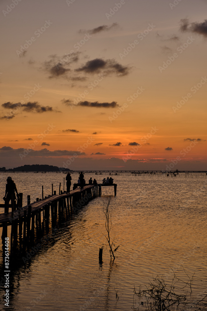 Fototapeta premium Golden hues of sunset paint the sky and reflect on the tranquil waters, creating a serene and picturesque scene by the pier