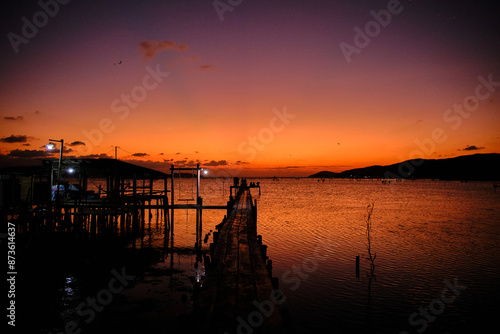 Golden hues of sunset paint the sky and reflect on the tranquil waters, creating a serene and picturesque scene by the pier