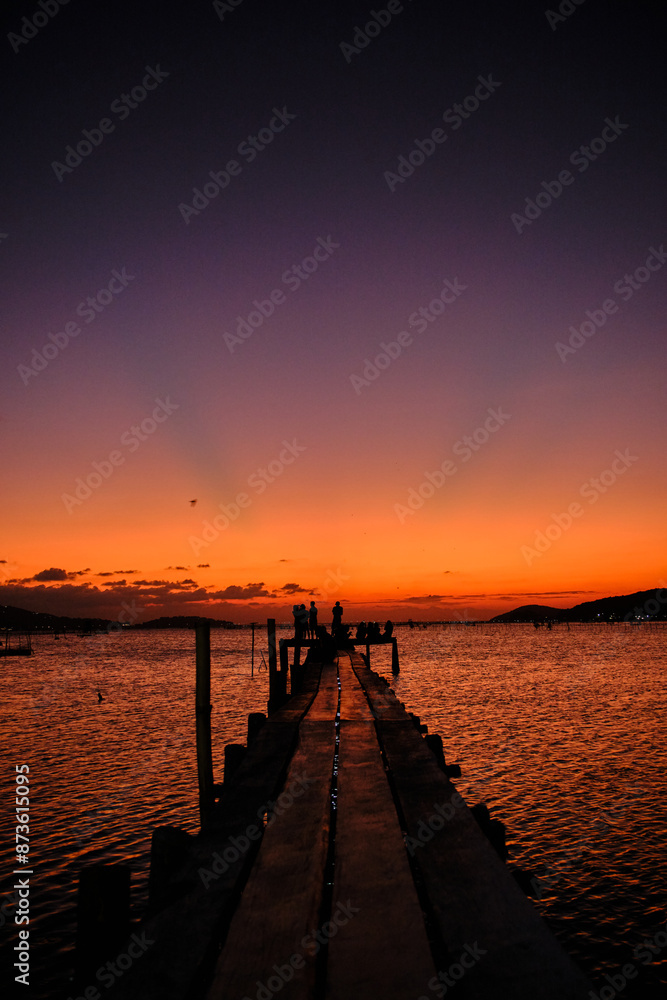 Fototapeta premium Golden hues of sunset paint the sky and reflect on the tranquil waters, creating a serene and picturesque scene by the pier
