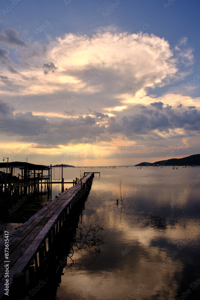 Golden hues of sunset paint the sky and reflect on the tranquil waters, creating a serene and picturesque scene by the pier Golden hues of sunset paint the sky and reflect on the tranquil waters, creating a serene and picturesque scene by the pier