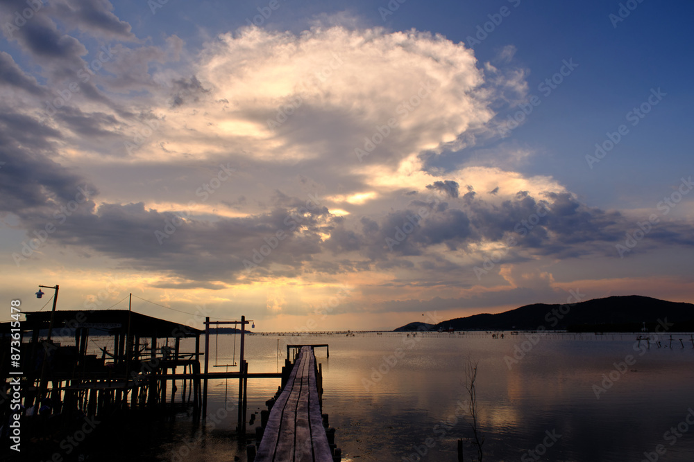 Obraz premium Golden hues of sunset paint the sky and reflect on the tranquil waters, creating a serene and picturesque scene by the pier
