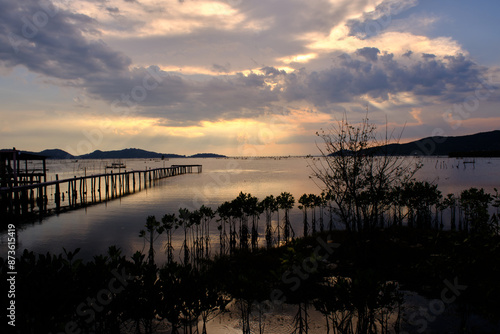 Golden hues of sunset paint the sky and reflect on the tranquil waters, creating a serene and picturesque scene by the pier