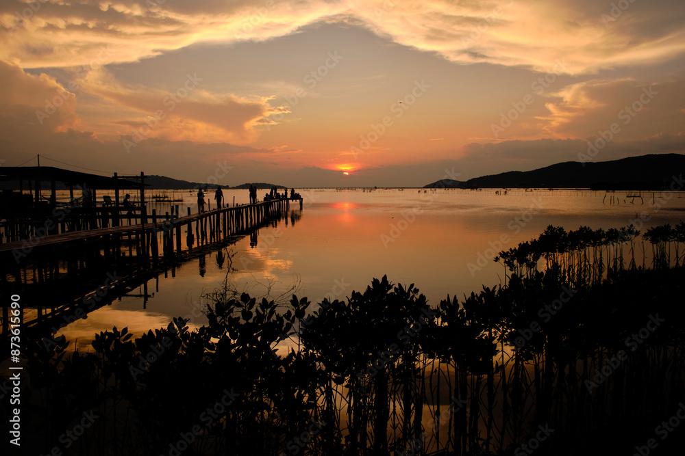 Golden hues of sunset paint the sky and reflect on the tranquil waters, creating a serene and picturesque scene by the pier Golden hues of sunset paint the sky and reflect on the tranquil waters, creating a serene and picturesque scene by the pier