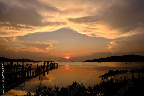 Golden hues of sunset paint the sky and reflect on the tranquil waters, creating a serene and picturesque scene by the pier