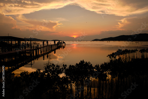 Golden hues of sunset paint the sky and reflect on the tranquil waters, creating a serene and picturesque scene by the pier