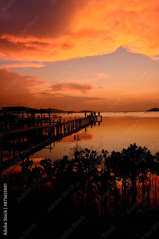 Obraz premium Golden hues of sunset paint the sky and reflect on the tranquil waters, creating a serene and picturesque scene by the pier
