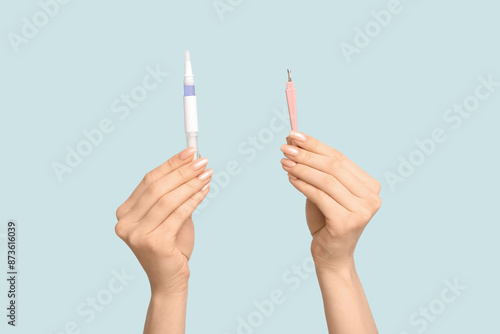 Female hands with cuticle oil pen and cutter on blue background