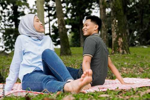 Young adult man and woman are enjoying picnic laying together on a blanket in a park. Summer picnic concept. Candid couple together enjoying time together.