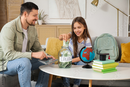 Father and his daughter putting money into jar with text COLLEGE at home. Tui...