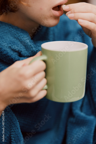 Woman sitting on couch with blanket over head holding coffee cup