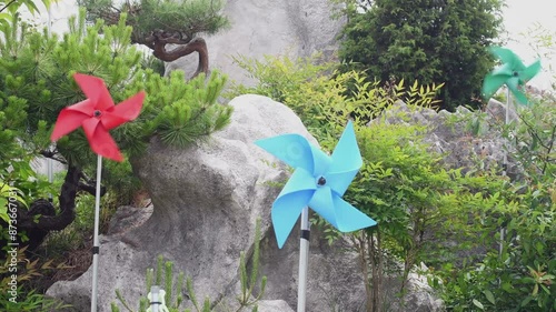 Pinwheels spinning in wind with background of boulders and green trees in urban park.