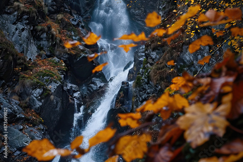 Scenic autumn waterfall surrounded by rocks and vibrant fall foliage, with orange leaves in the foreground, capturing the serene beauty and natural splendor of the fall season. photo