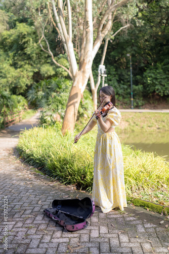 Tableau sur toile Young Chinese Malaysian woman in her 20s playing violin near a fountain pond in a large park in Bukit Jalik, Malaysia, wearing a yellow dress