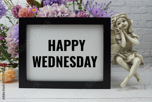 Happy Wednesday text with flowers and ceramic doll decoration on white brick wall and wooden background photo