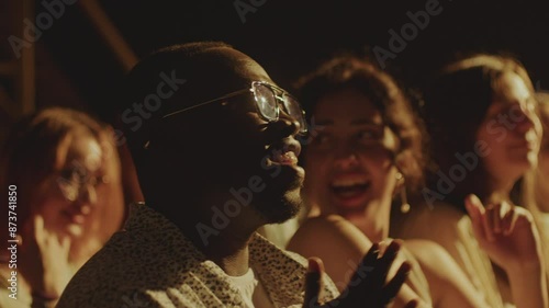 Young diverse people sitting in audience and laughing at jokes during stand-up show. Rack focus shot