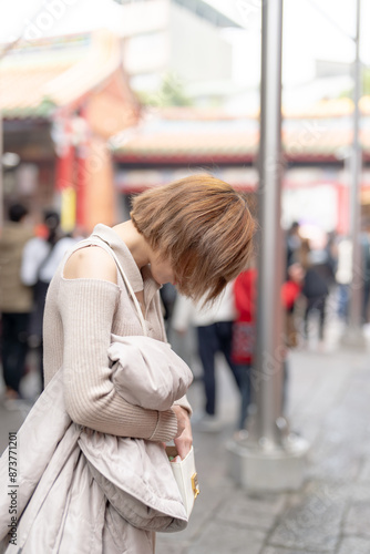 Young Taiwanese woman in her 20s wearing cream-colored clothes, performing Taiwanese-style prayers and divination at the famous tourist attraction Longshan Temple in Wanhua District, Taipei, Taiwan © HelloUG