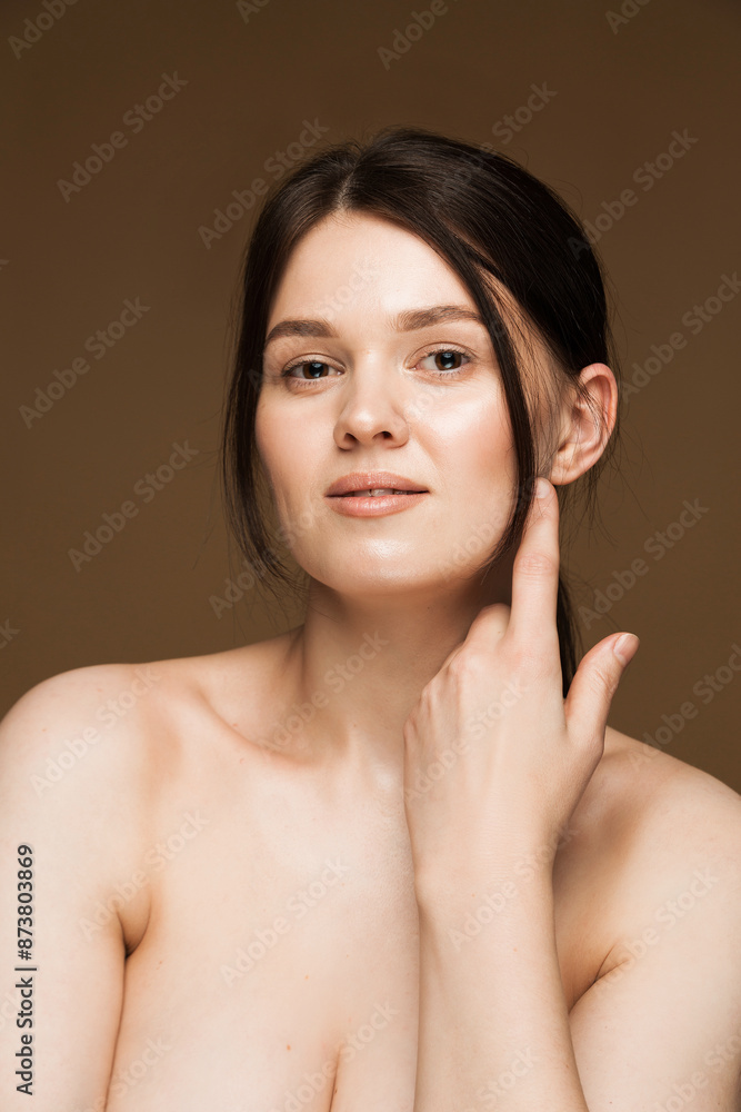 Brunette Woman with Bare Shoulders Touching Her Face on Brown Background. Portrait of a young brunette Caucasian woman with clear skin and bare shoulders, touching her face. Brunette Woman with Bare Shoulders Touching Her Face on Brown Background. Portrait of a young brunette Caucasian woman with clear skin and bare shoulders, touching her face.