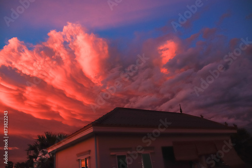 A dramatic summer sunset sky with orange and pink clouds over a house, creating a peaceful yet striking atmosphere