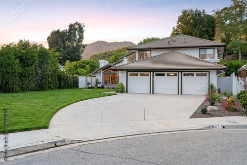 A suburban house with a three-car garage and well-maintained lawn at sunset