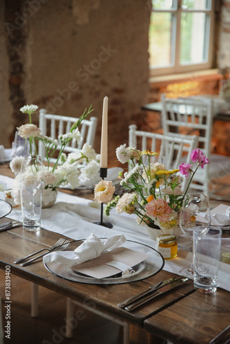 Rustic wedding table setting with white flowers and elegant candles, framed by natural light from a nearby window. photo