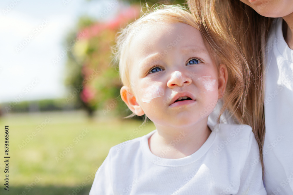 Sunscreen Spf 50. Toddler Female With Sunscreen Cream On Face On Bright Green Grassy Garden Background. Concept Of Baby Skin Protection From Uv Rays. Sunscreen Spf 50. Toddler Female With Sunscreen Cream On Face On Bright Green Grassy Garden Background. Concept Of Baby Skin Protection From Uv Rays.