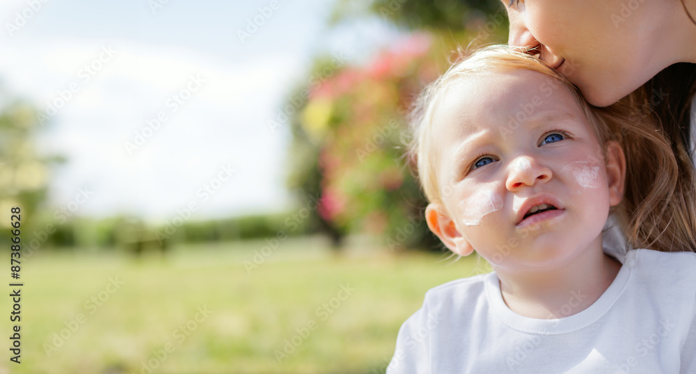 Young Mother Kissing Her Toddler Daughter On Green Grassy Garden. Concept Of Protecting Baby's Skin From Uv Rays. Concept Of Skin Cancer Prevention And Aging. Sunscreen On The Face. Child Taking Care Young Mother Kissing Her Toddler Daughter On Green Grassy Garden. Concept Of Protecting Baby's Skin From Uv Rays. Concept Of Skin Cancer Prevention And Aging. Sunscreen On The Face. Child Taking Care