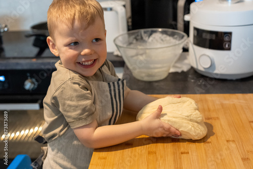 Little baby boy in a suit of the cook sculpts dough. Small kid scullion make dinner in chef suit. Cooking child lifestyle concept. Toddler enjoy, having fun, learning and playing in the kitchen. High photo