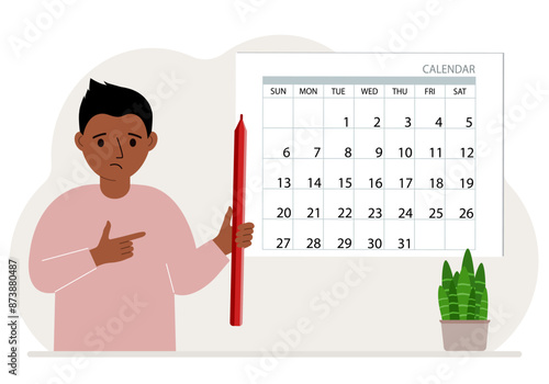 The boy holds a red pencil and stands near a large calendar.