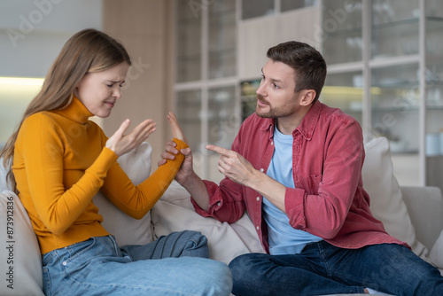 Married spouses, husband, wife sort things out. Serious man swearing sternly at saddened woman. Unhappy upset girl cannot hold back tears. Abusive relationship, domestic quarrel, family troubles. photo