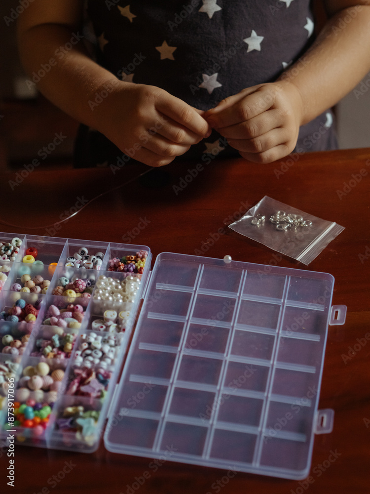 Kid Craft with Beads: A vertical close-up shot captures a toddler girl’s hands creating bead jewelry. Kid Craft with Beads: A vertical close-up shot captures a toddler girl’s hands creating bead jewelry.
