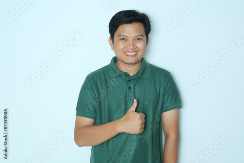 Young Asian man smiles and gives a thumbs up to the camera. Wearing a green t-shirt photo