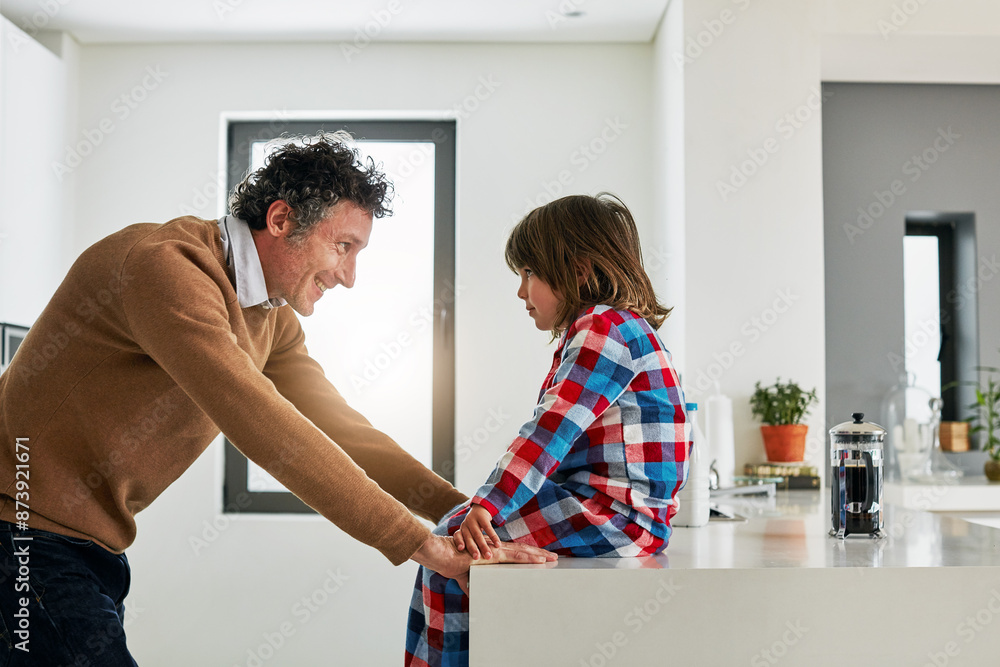 Obraz premium Dad, boy and kitchen for conversation in home, smile and love for discussion with child. Coffee, morning and pajamas for breakfast and talking with father person, cooking or bonding for nutrition