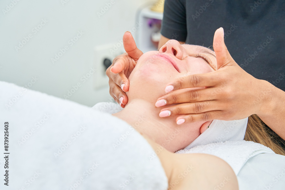 A woman is receiving a facial treatment from a woman. The esthetician slides her hands with oil over her neck. A woman is receiving a facial treatment from a woman. The esthetician slides her hands with oil over her neck.