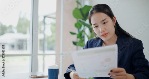 Portrait of Asian businesswoman in suit drink coffee while analyze documents and taking notes in small coffee shop. Work from anywhere, Remote working