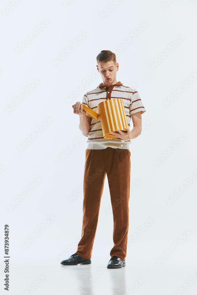 Stylish young man in retro style clothes, pants and shirt, opening cardboard present box with impressive face isolated on white background. Surprise. Retro style, 1950s, celebration, emotions concept Stylish young man in retro style clothes, pants and shirt, opening cardboard present box with impressive face isolated on white background. Surprise. Retro style, 1950s, celebration, emotions concept