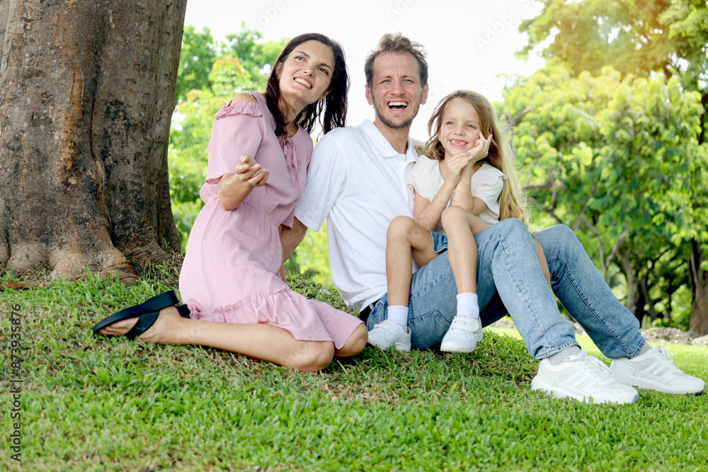 Portrait of happy beautiful family in outside garden. Joyful parents and daughter girl relaxing during sitting under tree at green park. Father, mother, and kid child spending time together outdoor. Portrait of happy beautiful family in outside garden. Joyful parents and daughter girl relaxing during sitting under tree at green park. Father, mother, and kid child spending time together outdoor.