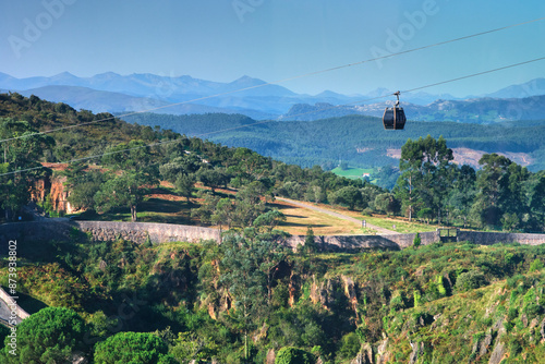 A cable car is flying over a mountain. The sky is clear and blue.