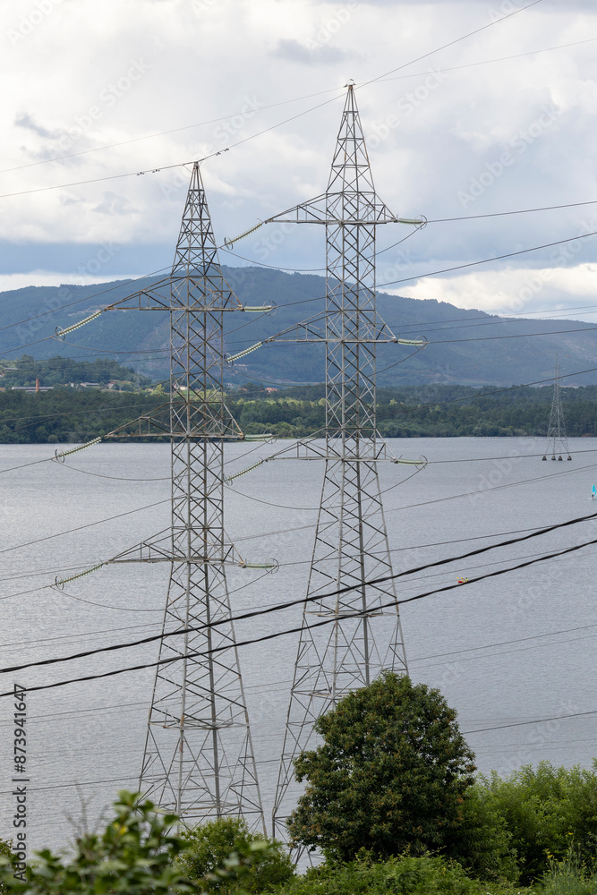 A tall metal transmission tower carries multiple high voltage power ...