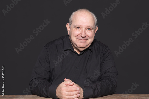 Portrait of a sexagenarian man with white hair and black shirt posing smiling looking at camera. Copy Space. Concept of aging