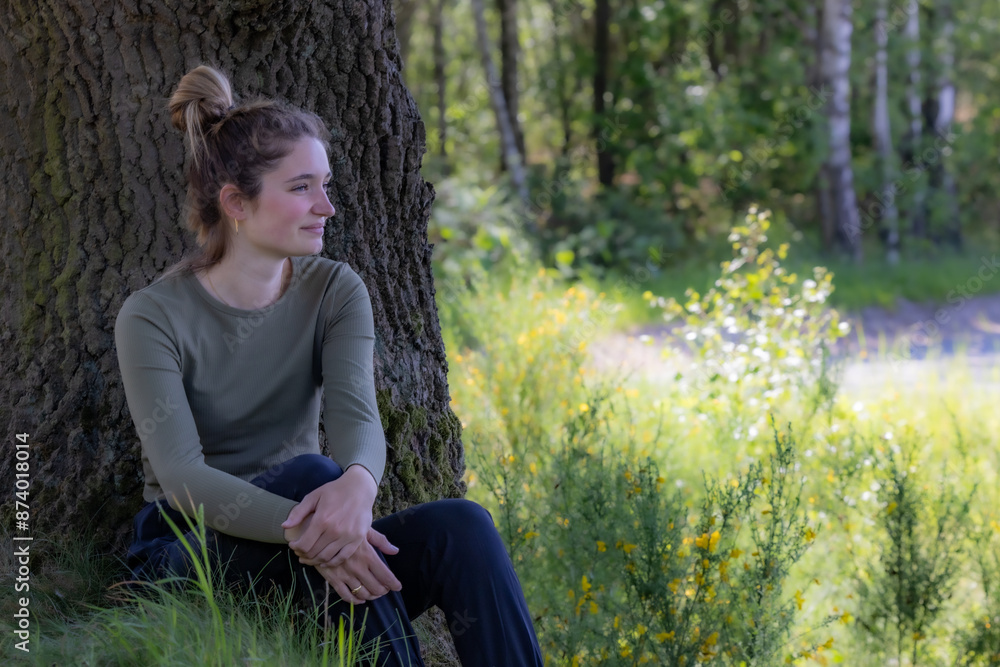 A young woman sits under a tree, finding peace and calm in the serene natural beauty on a sunny day A young woman sits under a tree, finding peace and calm in the serene natural beauty on a sunny day
