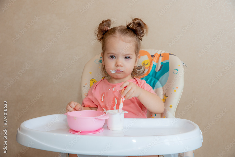 A little girl is sitting on a high chair eating at home A little girl is sitting on a high chair eating at home