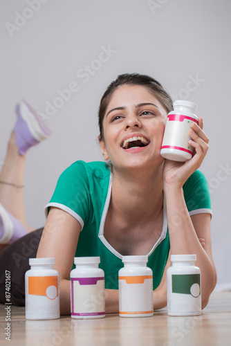 Smiling Indian Fashion Woman Lying Down On Floor Holding Bottle Of Pills In Hand
