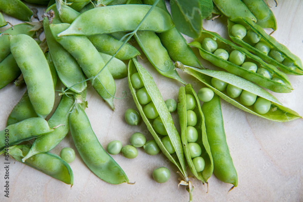 Freshly gathered pea pods , some open with seeds visible, on a wooden tray Freshly gathered pea pods , some open with seeds visible, on a wooden tray