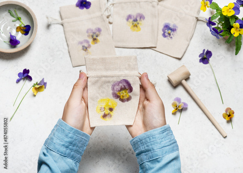 View from above of a small handmade fabric bag with hammered pansy flower prints. Step by step of creating a cloth bag with flower prints. Natural material craft for kids concept.