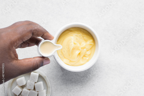 Overhead view of milk being poured on nigerian akamu in a white bowl, pap akamu or ogi in a white bowl, top view of nigerian corn pudding in a white ramekin photo